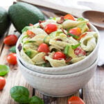 A bowl of salad, with pasta, avocado and tomatoes