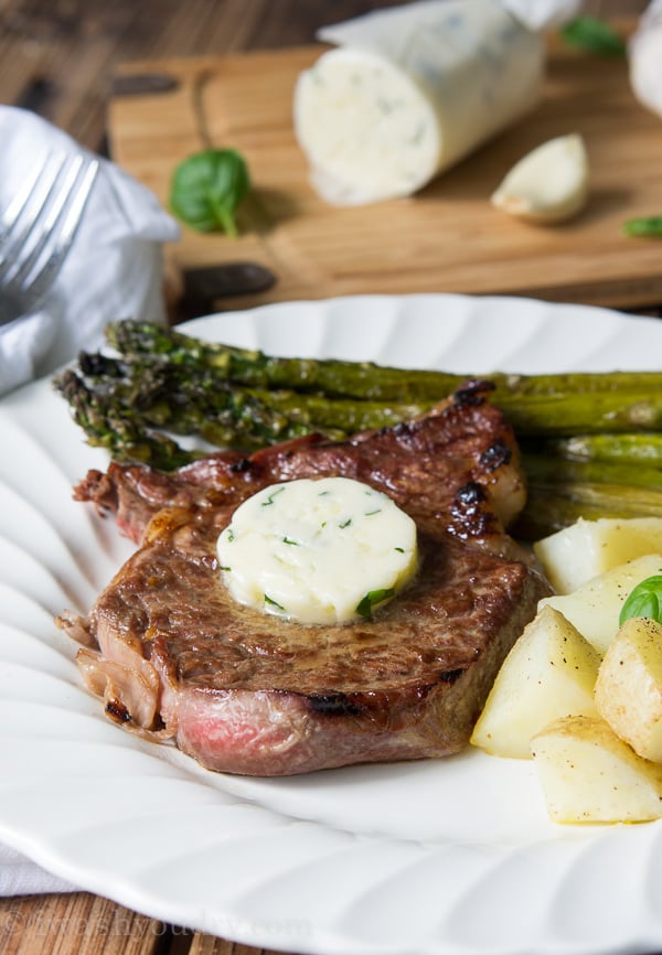 A close a plate with a steak and melting butter with a side of asparagus and potatoes 