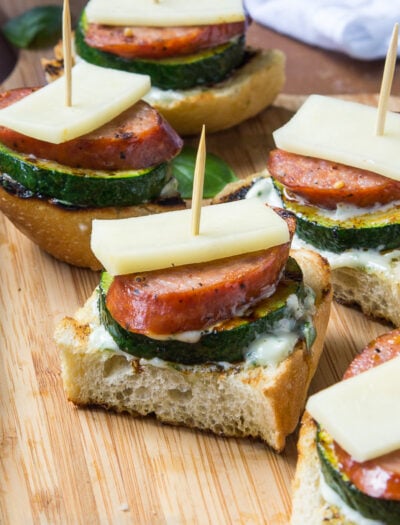 Bread squares with sliced veggies, meat and cheese on top put together with a toothpick.