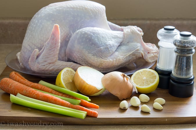 Raw turkey on a pan on a table, surrounded by onions, lemons, carrots and celery