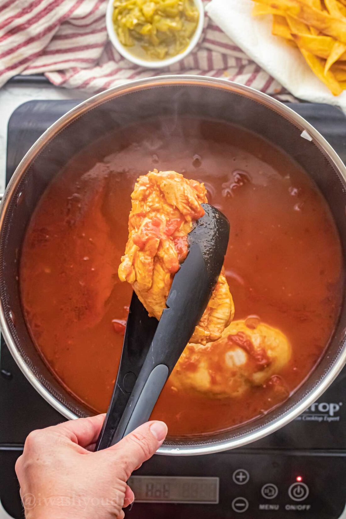 Black tongs lifting cooked chicken out of soup pot. 