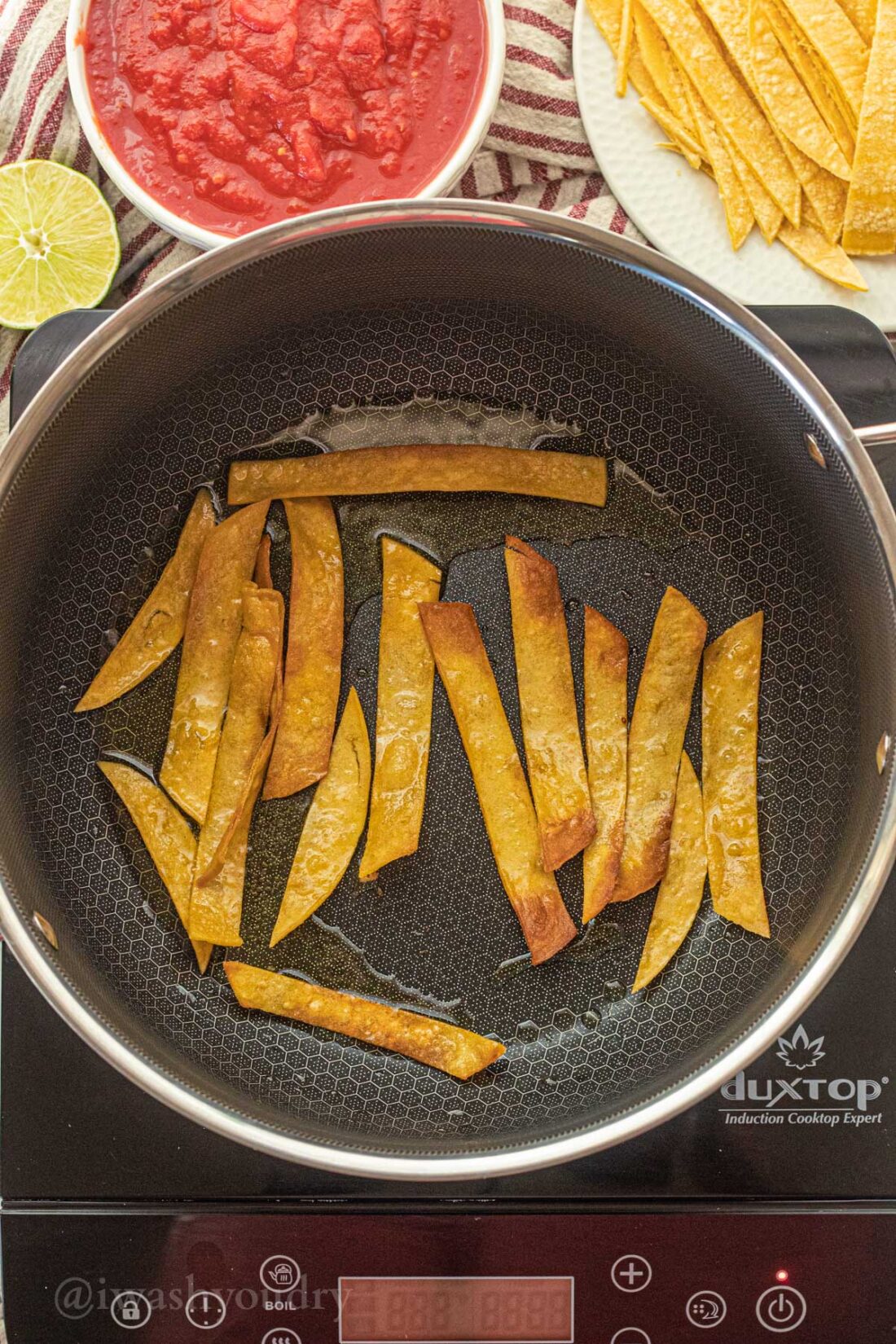 Corn tortilla strips frying in black pan with olive oil. 