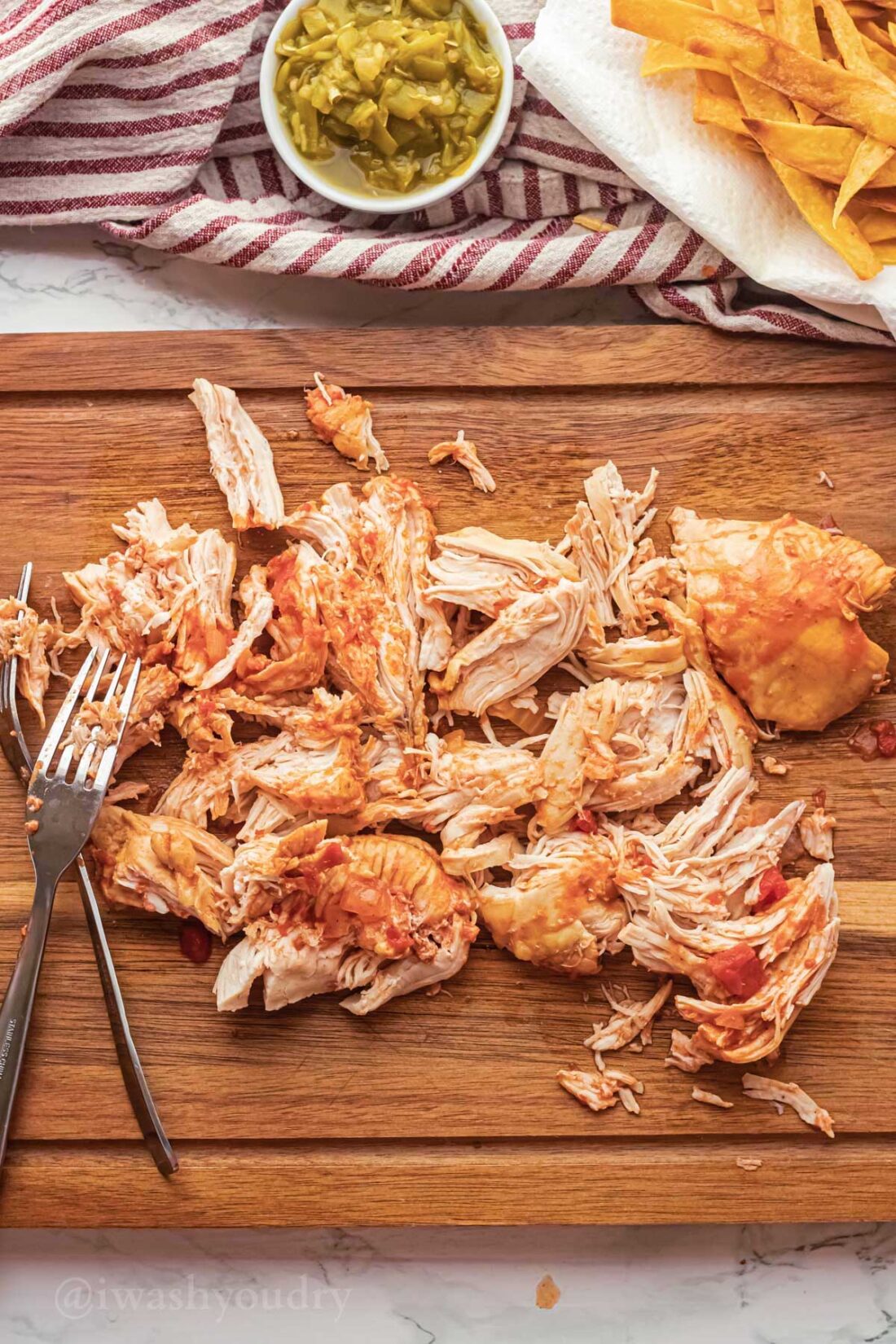Shredded cooked chicken on wood cutting board. 
