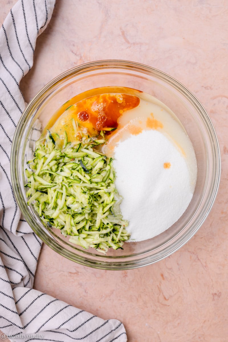 Wet ingredients for zucchini bread in clear glass bowl with a dish towel. 