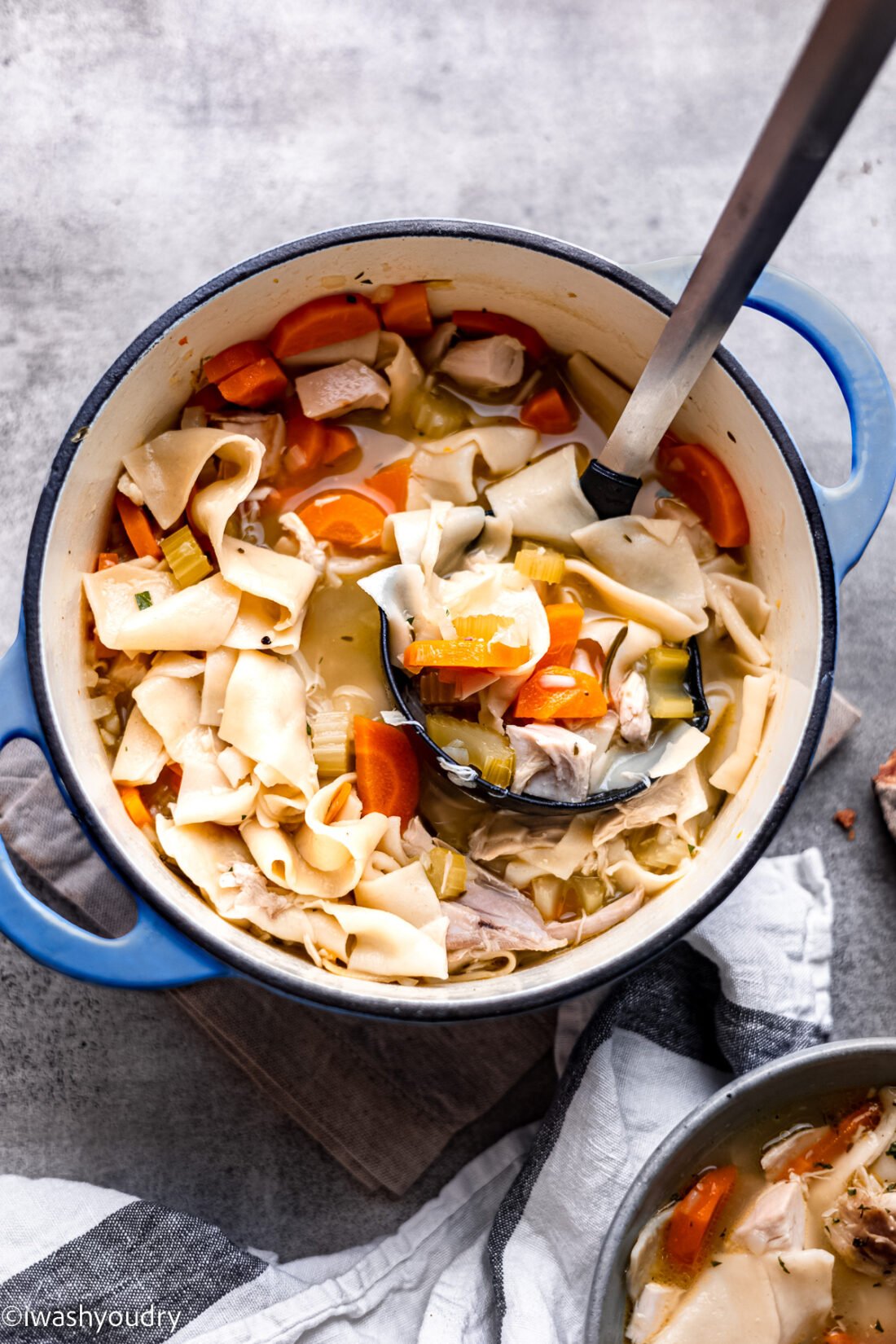 Cooked turkey noodle soup in blue pot with dish towel. 