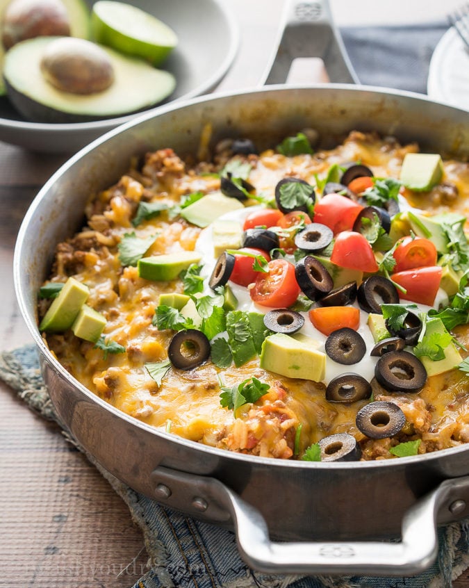 skillet with cooked beef and rice with avocado, tomato and sour cream