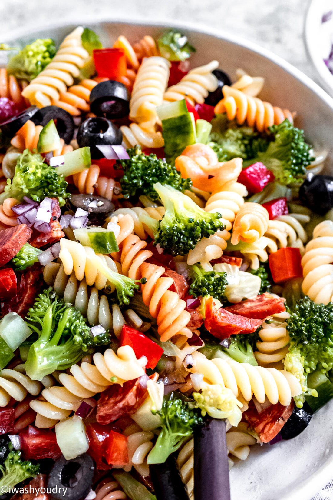 Easy Italian Pasta Salad recipe in bowl with twirly pasta, bell peppers, olives and broccoli.