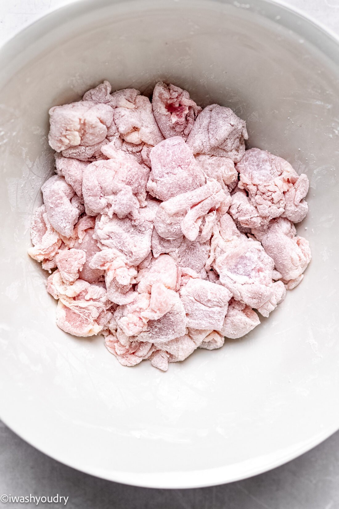 Coated raw chicken in a white bowl. 