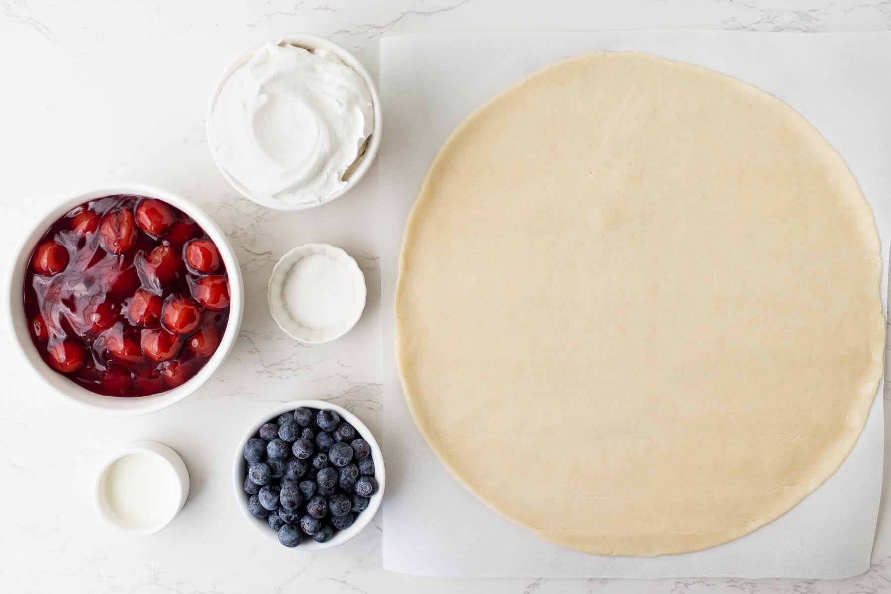ingredients for cherry galette on white surface with cool whip, cherries and blueberries.