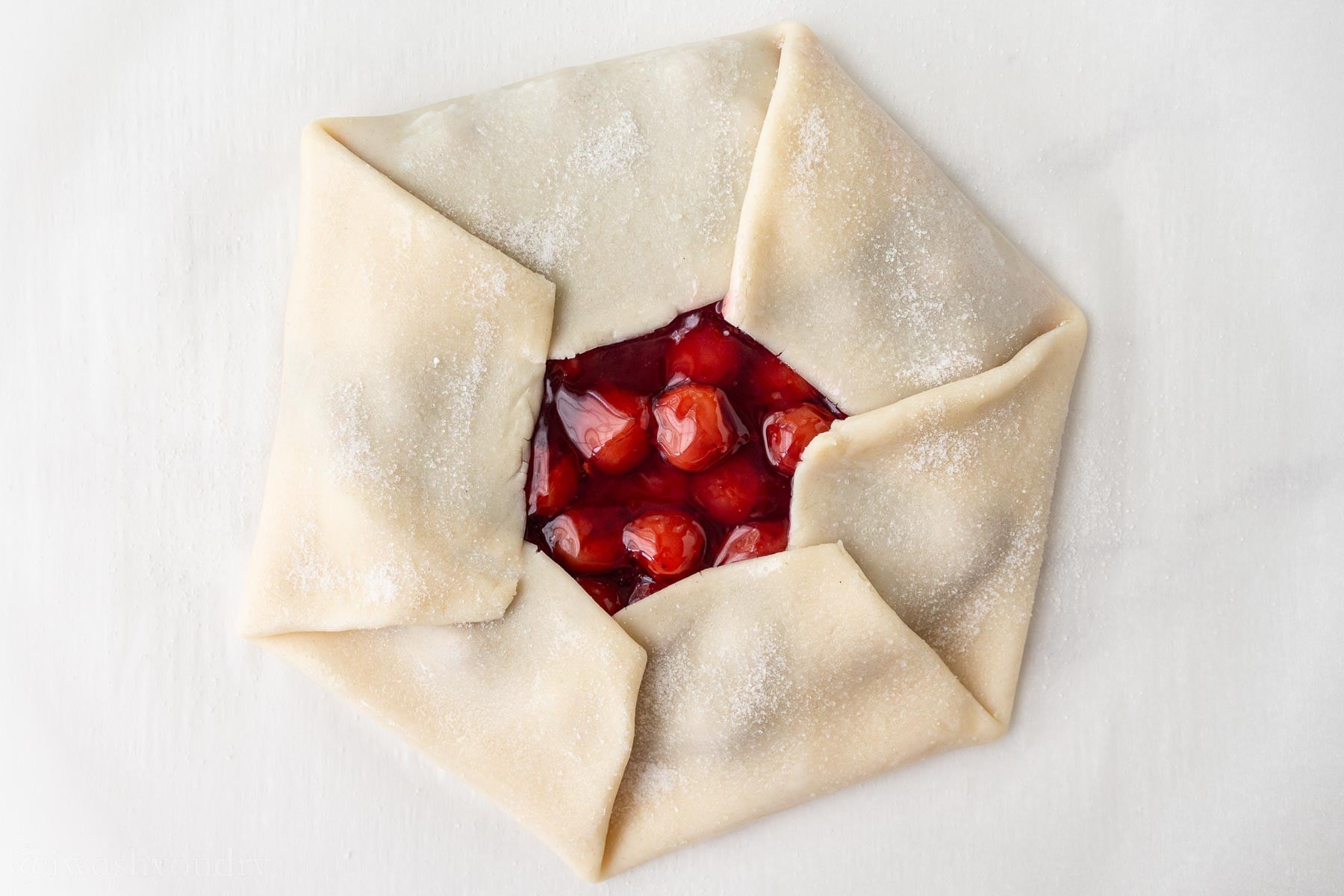 Cherry pie filling peeking out of the pie crust with folded edges.