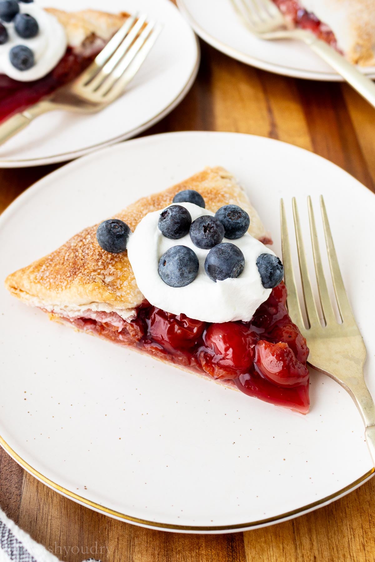 sliced cherry galette with cool whip and blueberries on top.