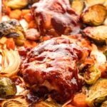 Baked bbq chicken on metal sheet pan with carrots and brussels sprouts.