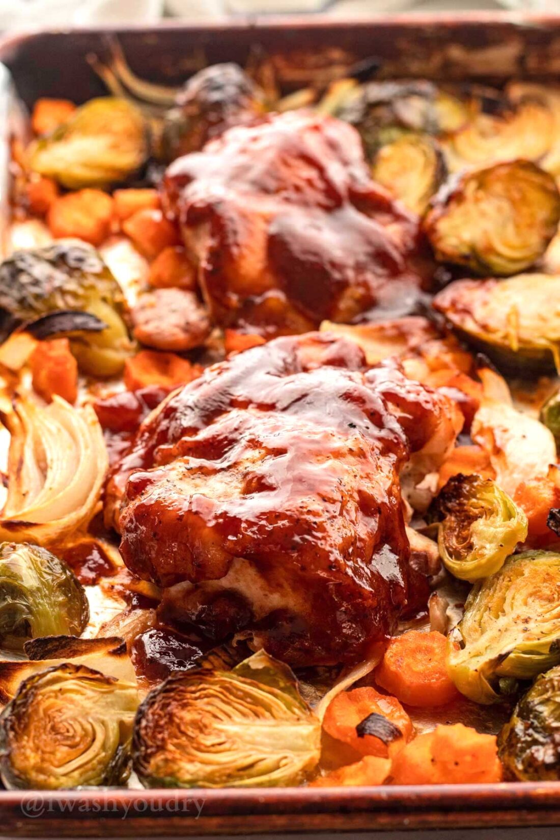 Baked bbq chicken thigh with carrots and brussels sprouts on metal baking pan. 