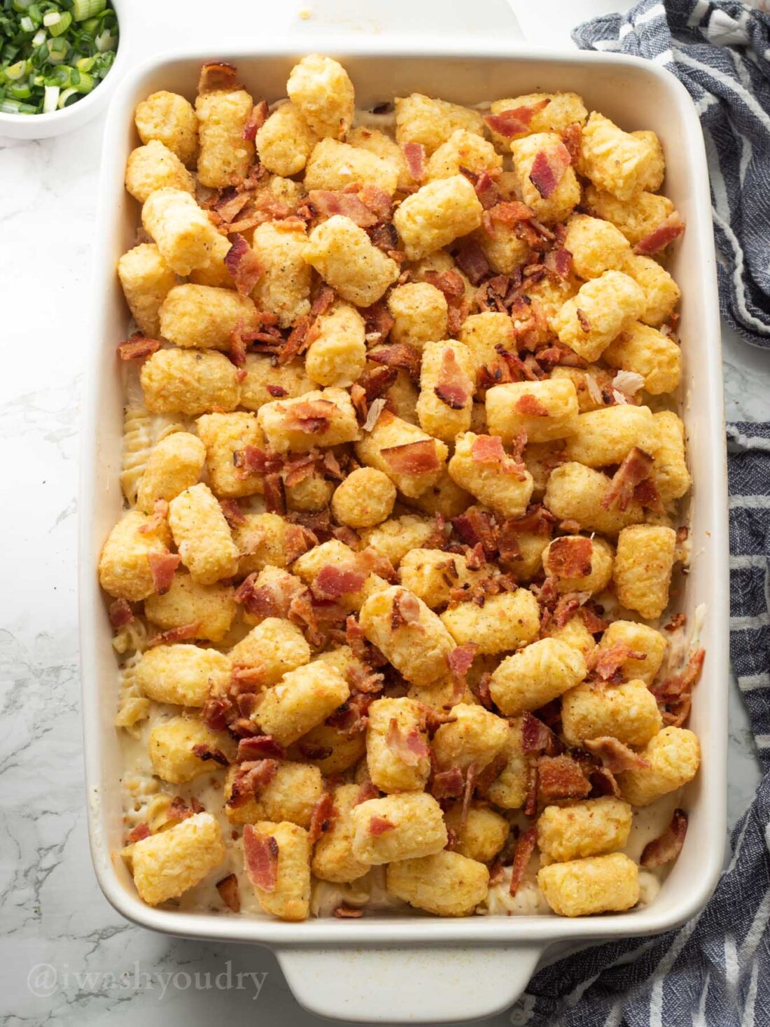 Unbaked tater tot chicken casserole with bacon in white casserole dish. 