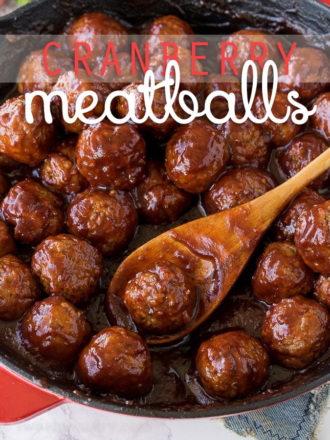 cranberry meatballs in skillet with wooden spoon and sauce.