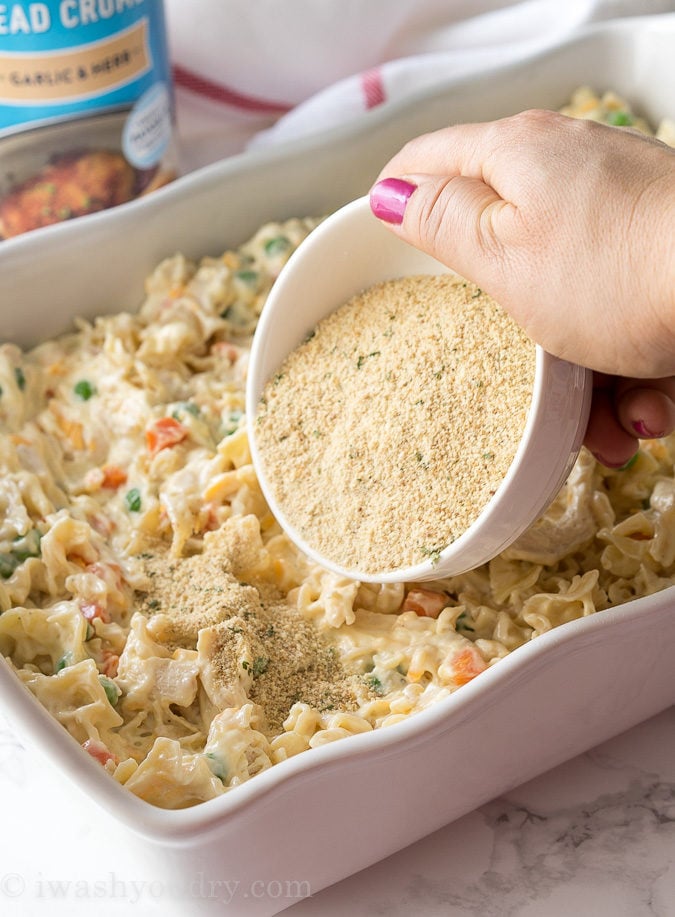 pouring crumb topping over casserole dish with noodles.
