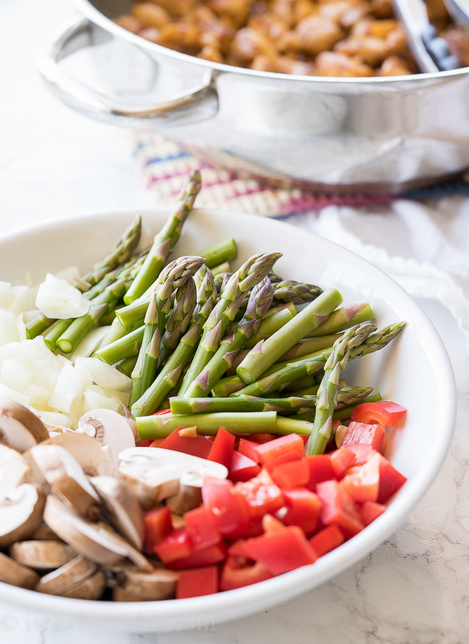 vegetables in white bowl with asparagus and red peppers.