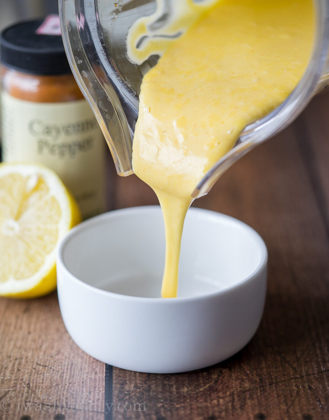 pouring yellow hollandaise sauce in white bowl with lemon