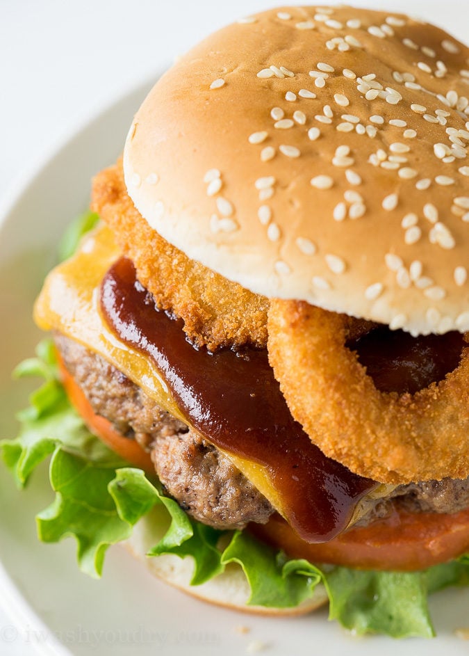 burger with sauce and onion rings on white plate.