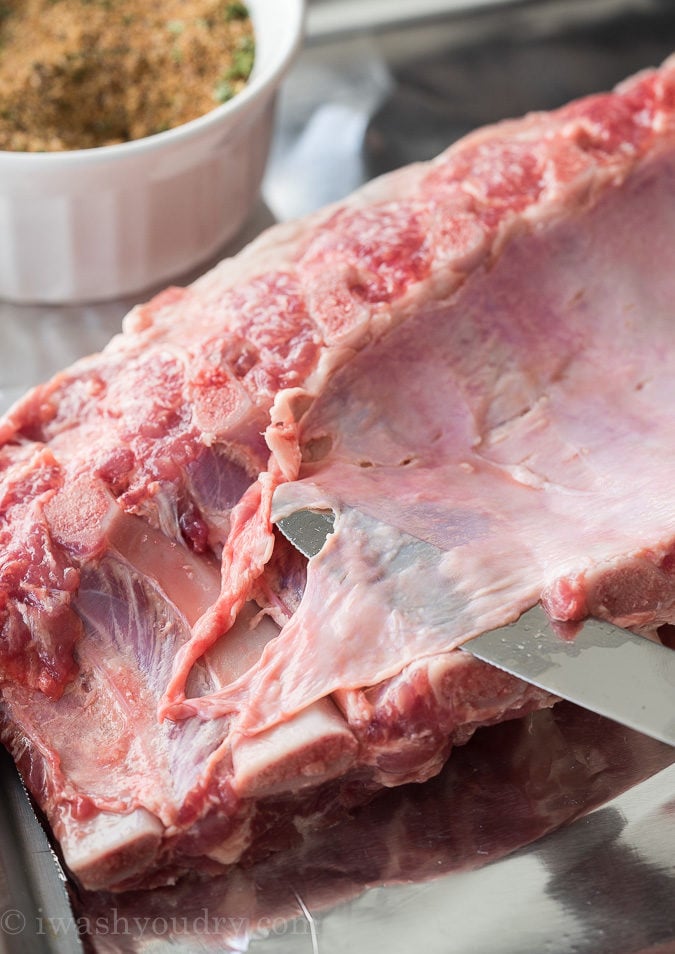 When making ribs, the first thing you want to do is remove the skin on the underside of the bones. Run a butter knife underneath the skin to loosen it.