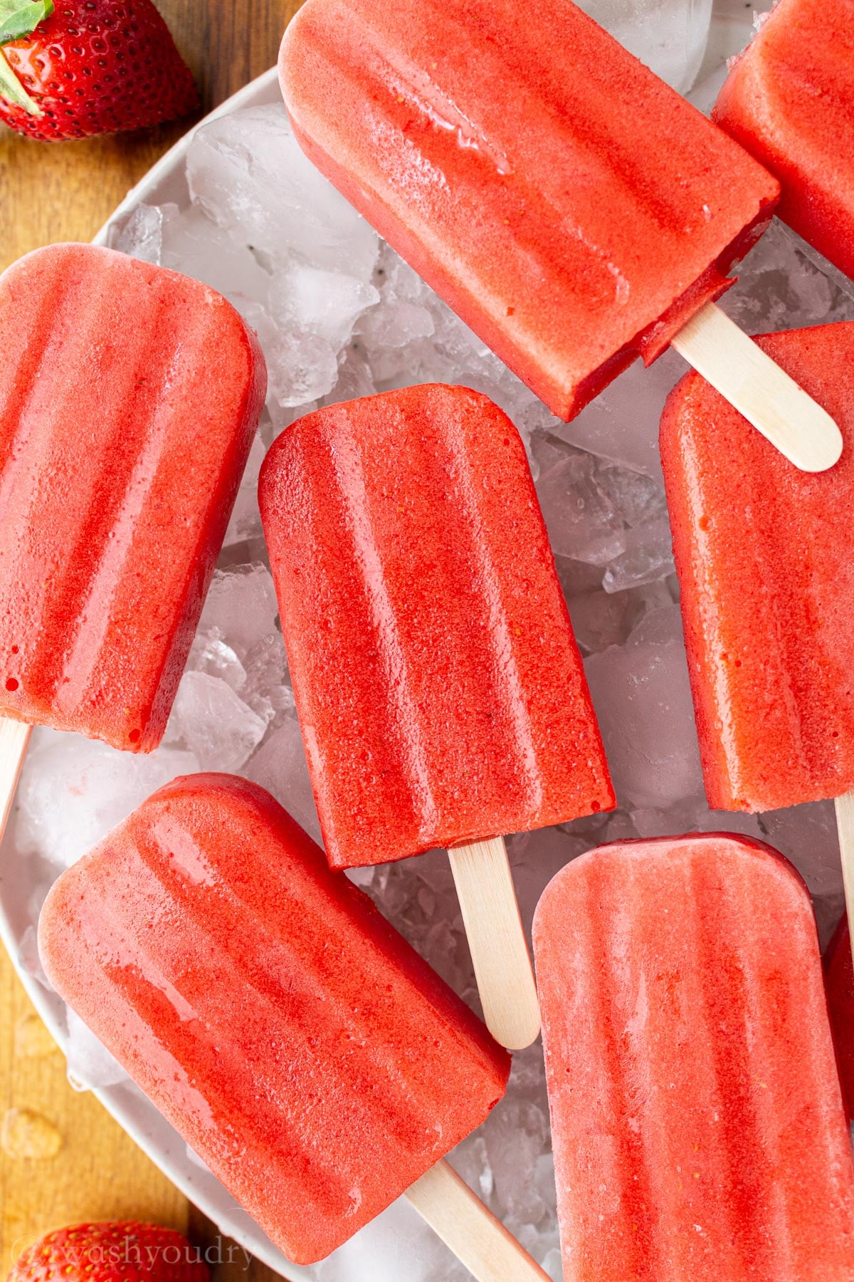 fresh strawberry and pineapple popsicles on a bed of ice cubes.