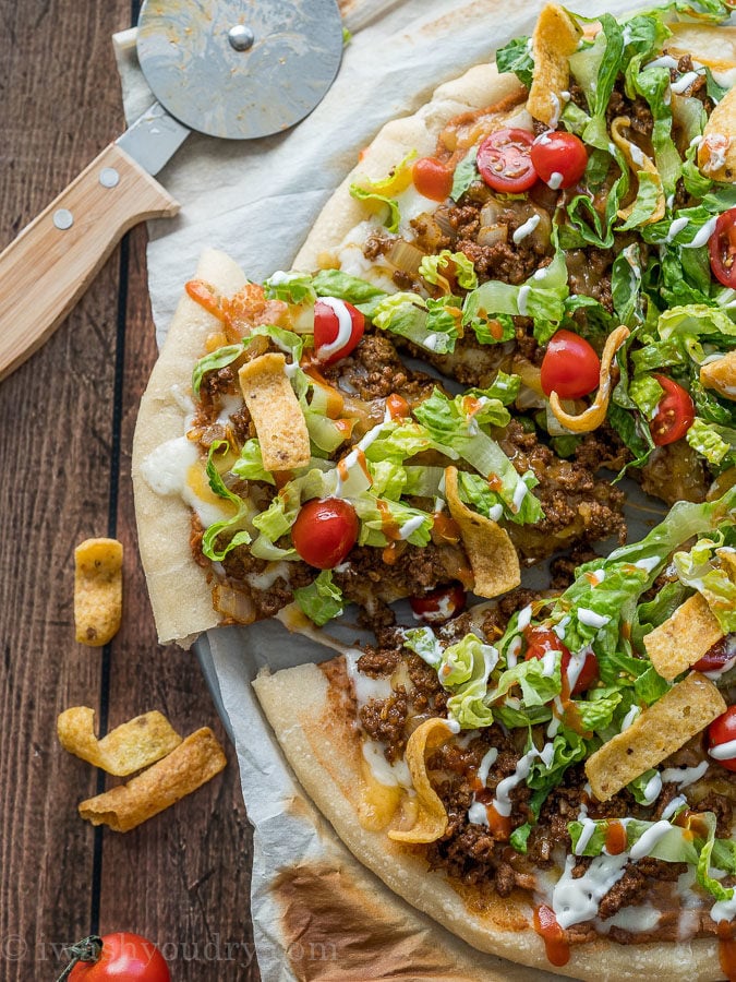 Sliced Taco Pizza with pizza cutter and corn chips on the side.