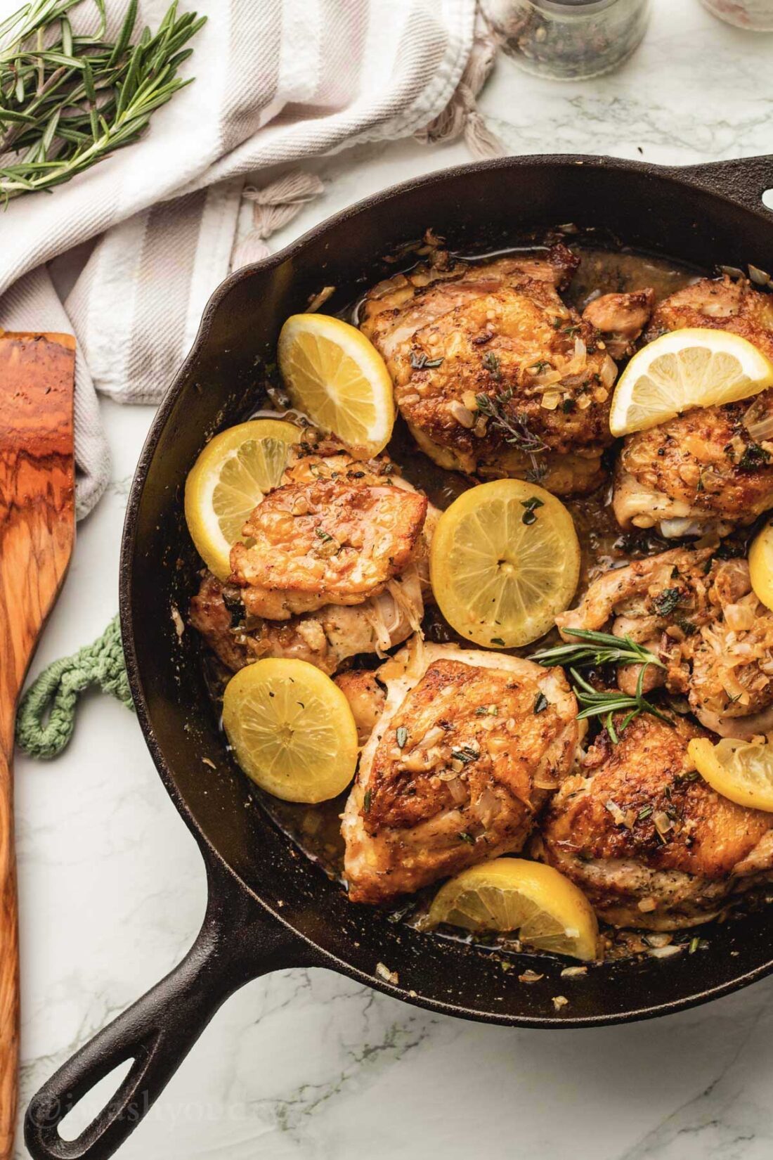 black skillet with roasted garlic and herb chicken thighs in it, with added lemon slices.