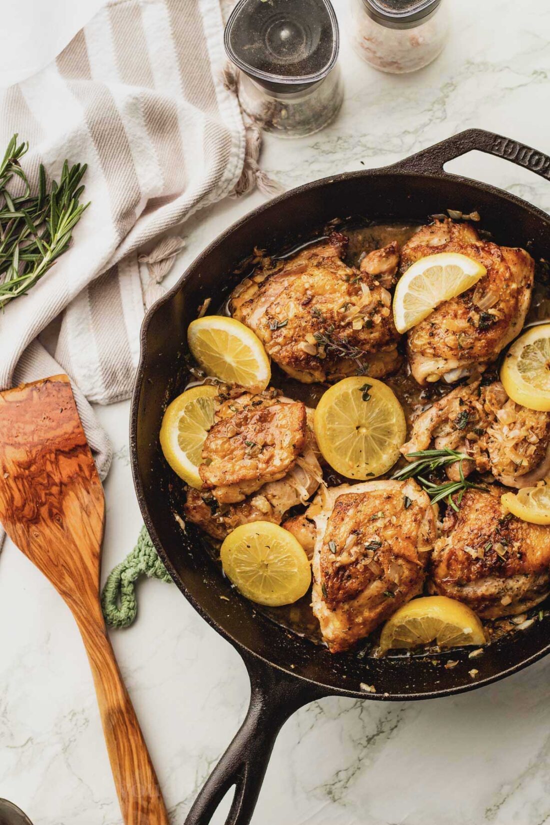 garlic and herb chicken thighs in pan with lemon slices on top.