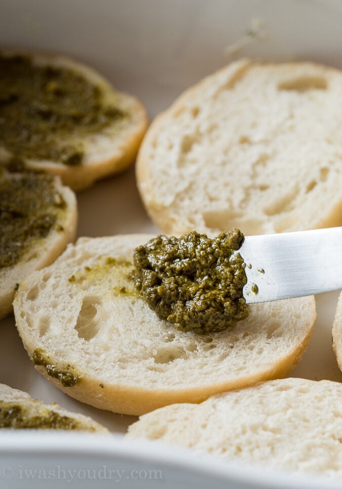 Spread a little bit of basil pesto over the bottom half of each savory garlic knot and place in a baking sheet.