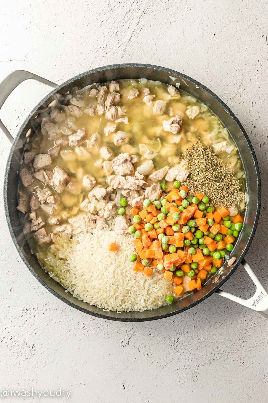 Cooked pork with rice, peas, and carrots in a skillet. 