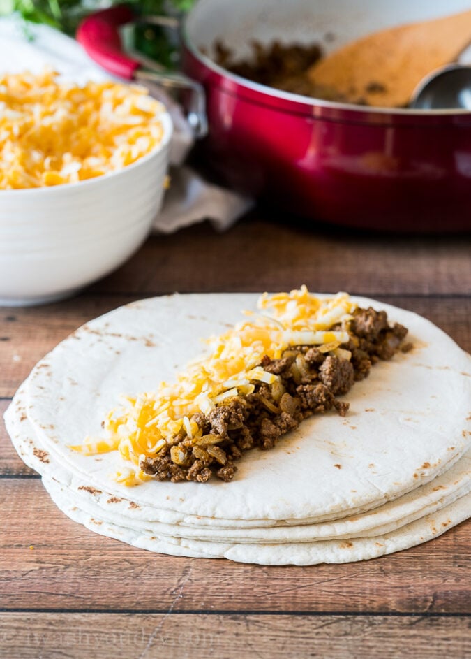 To start making these ground beef enchiladas, start by adding about 1/3 cup of seasoned ground beef and cheese to the center of a small tortilla, then roll up and place in your 9x13 inch casserole dish.