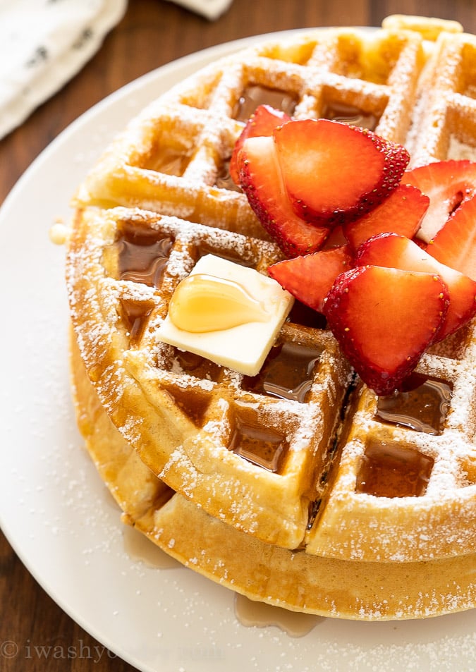 Crispy waffles on white plate with syrup and strawberries.