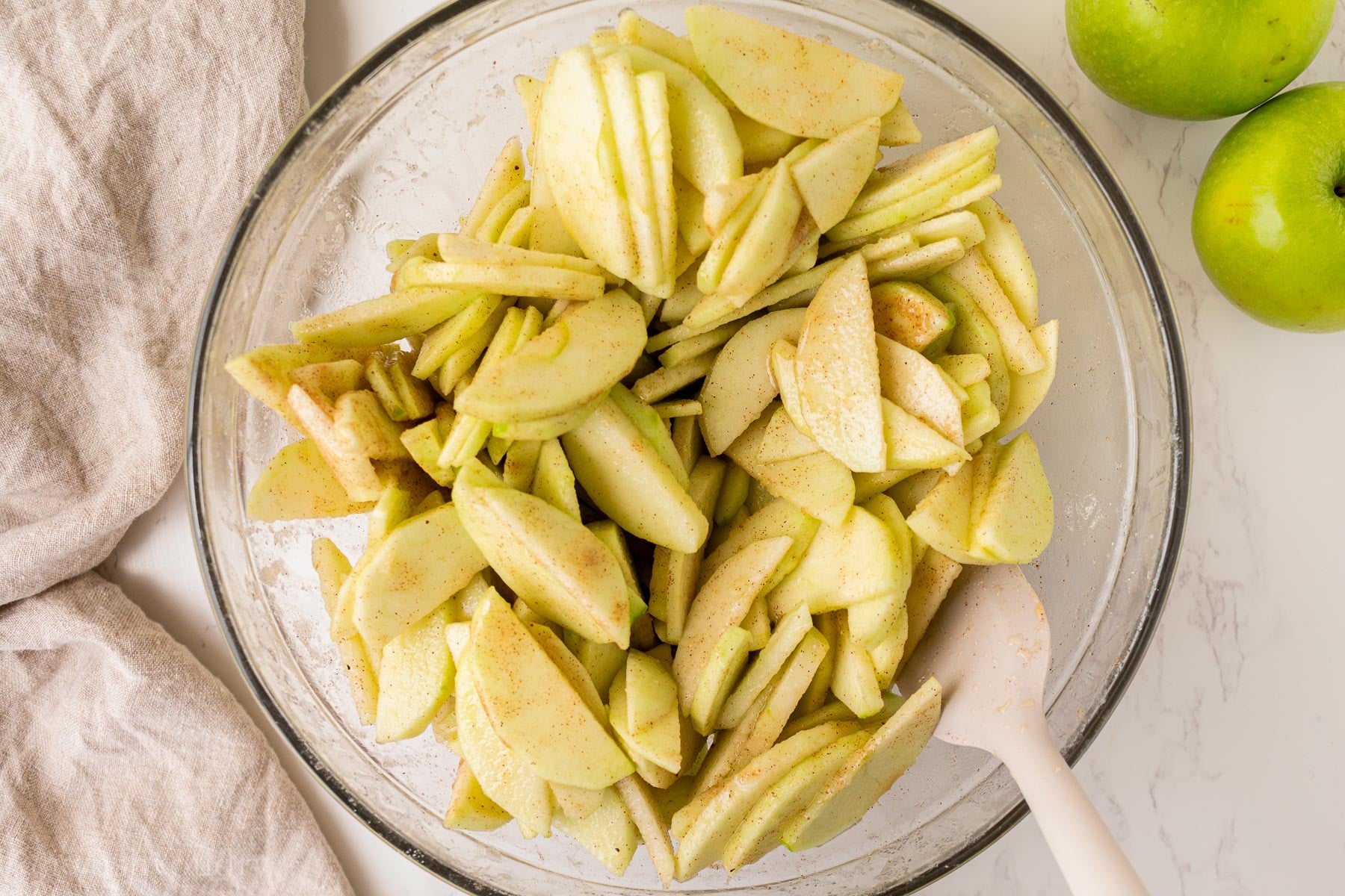 apple slices and spices mixed together with apple juice concentrate in glass bowl.