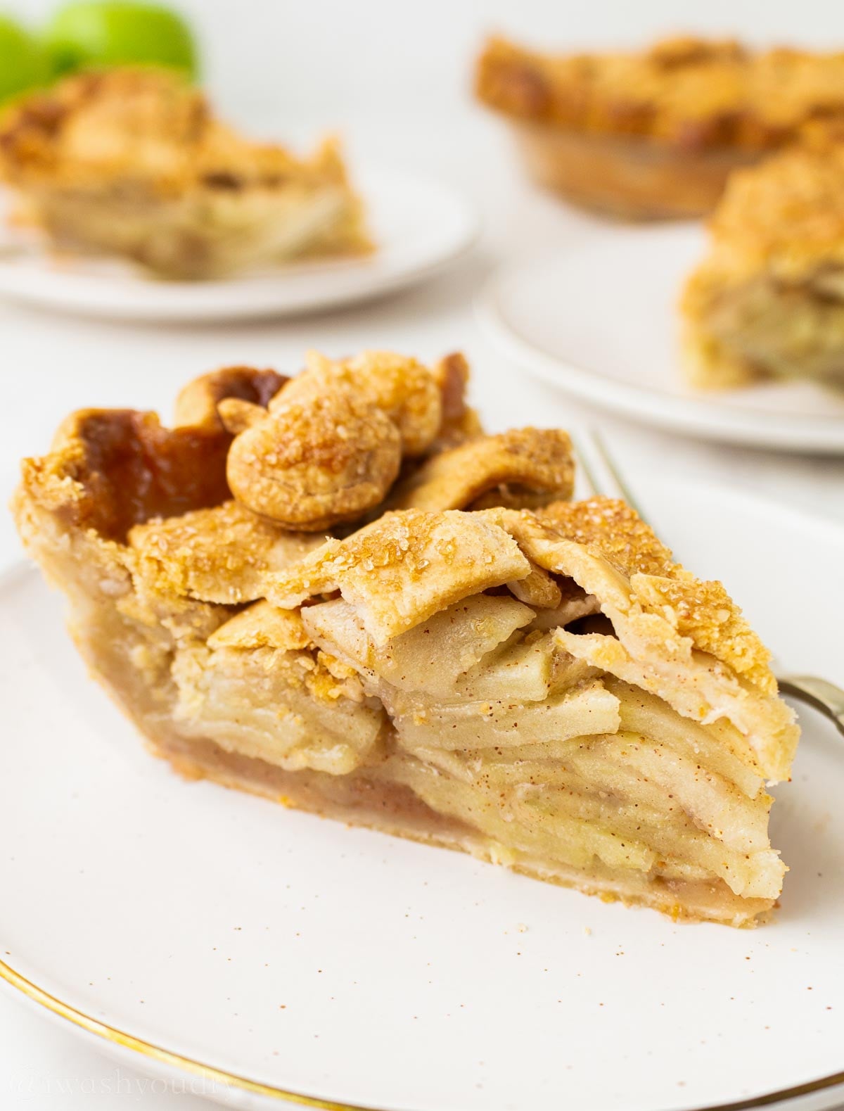 slice of apple pie on white plate with golden brown pie crust on top.