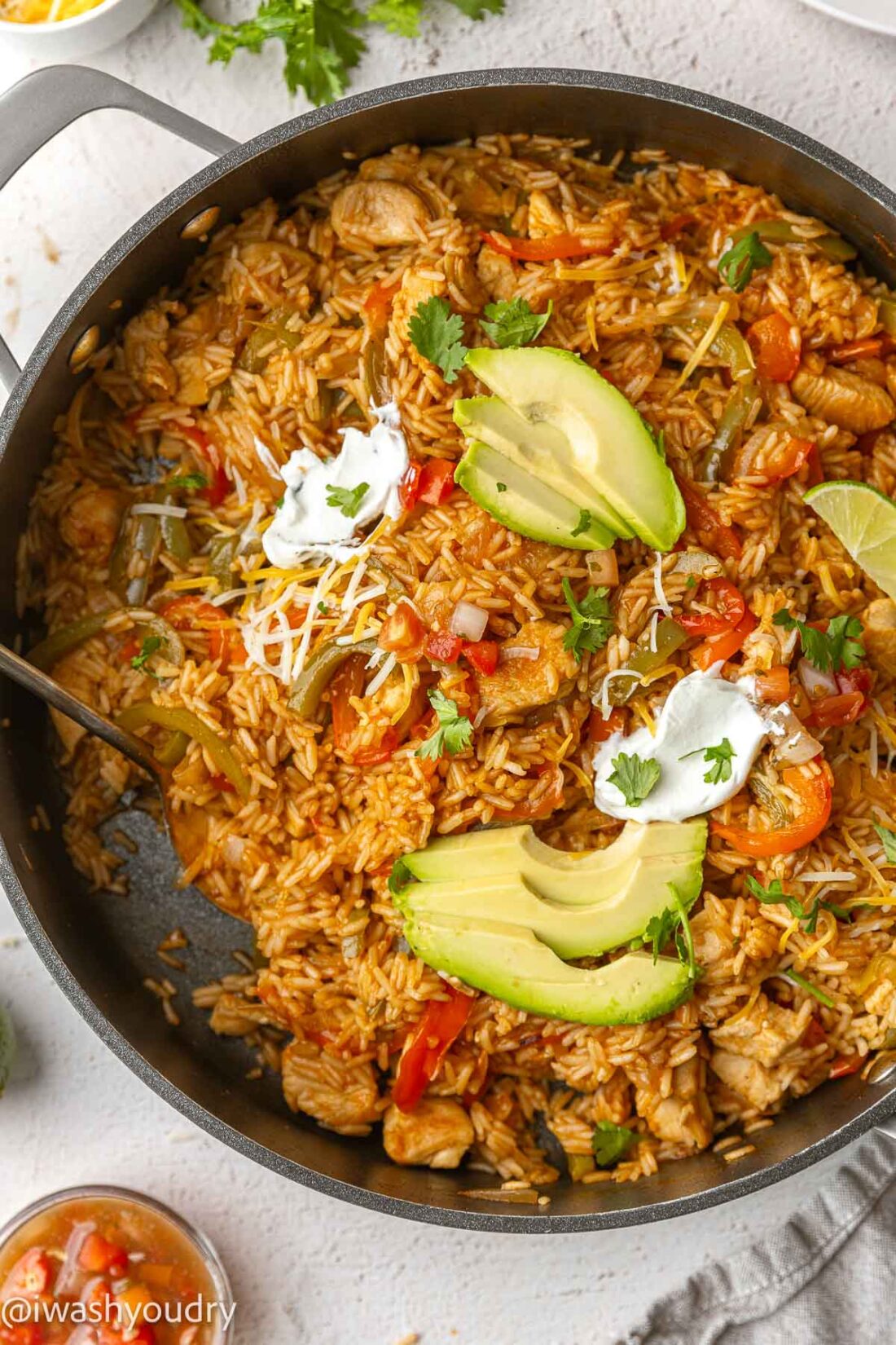 large black skillet filled with fajita rice, chicken and peppers. Topped with cheese and avocado slices.