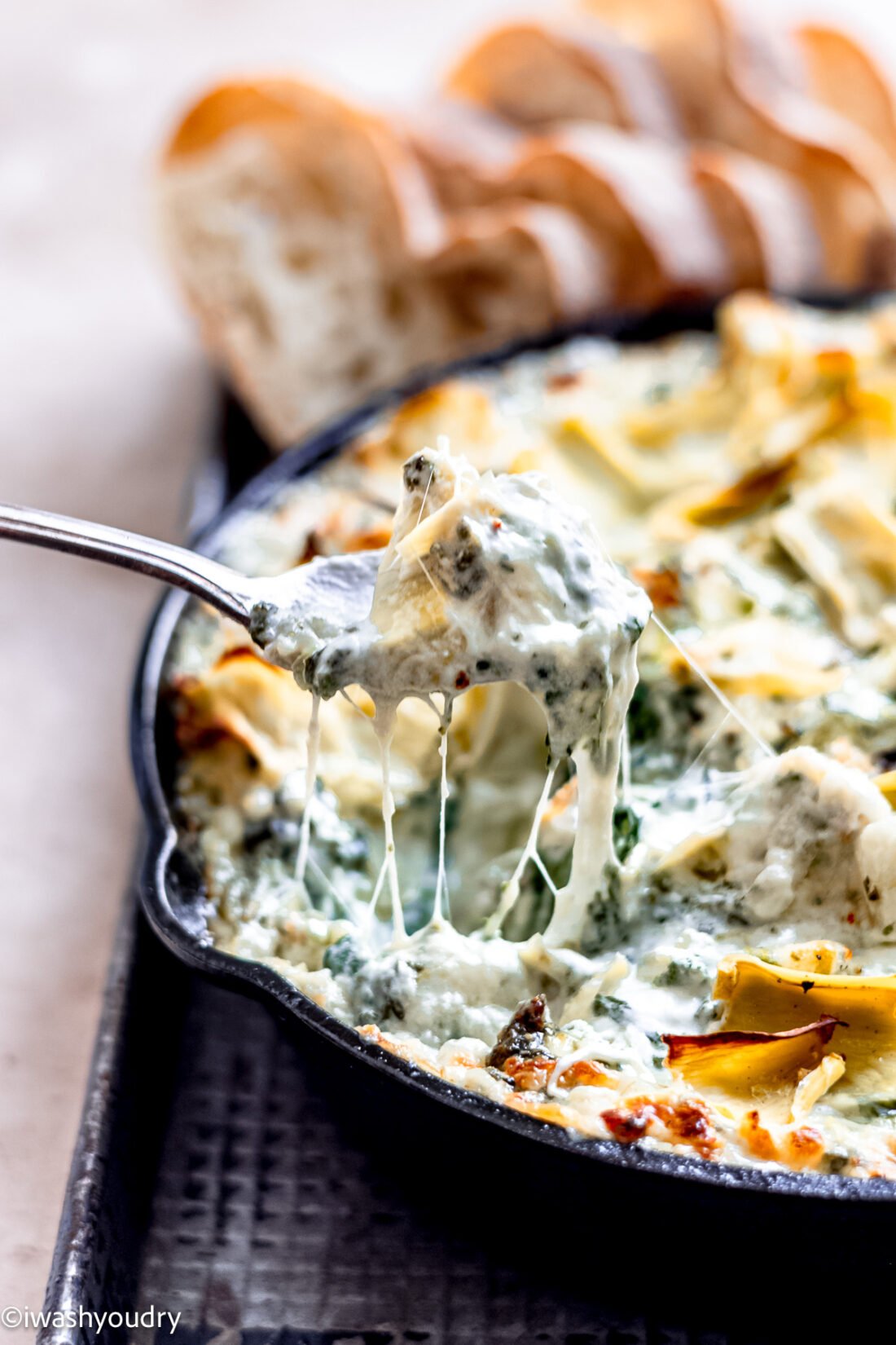 Spoon lifting baked spinach artichoke dip from pan. 