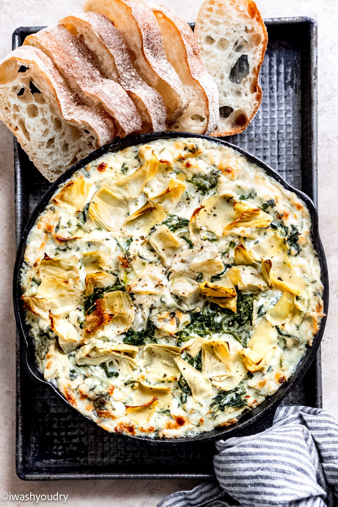 Black pan of spinach artichoke dip with bread on side. 