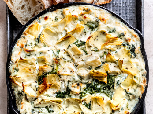 Black pan of spinach artichoke dip with bread on side.