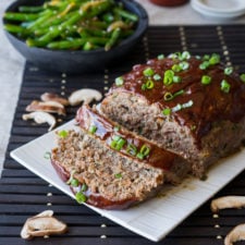 A meat loaf on a serving plate with slices taken and a side bowl of asparagus