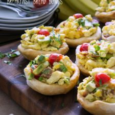 A close up of mini breakfast bread bowls with bacon, egg and cheese topped with veggies