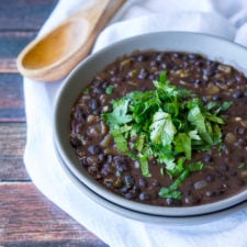 A bowl of food on a plate, with black beans and topped with herbs