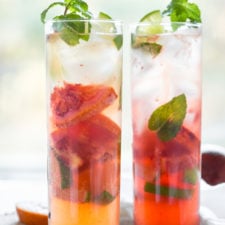 A close up of drinks with ice, fruit and leaves in two glasses