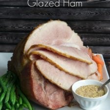 A spiral sliced ham on a serving platter with a side of green beans and a bowl of brown sugar and balsamic glaze