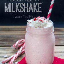 A glass jar filled with Candy Can Crunch Milkshake topped with whipped cream and crushed candy cane and a red and white straw