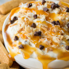 A close up of a bowl of cookie dip topped with  caramel and chocolate chips