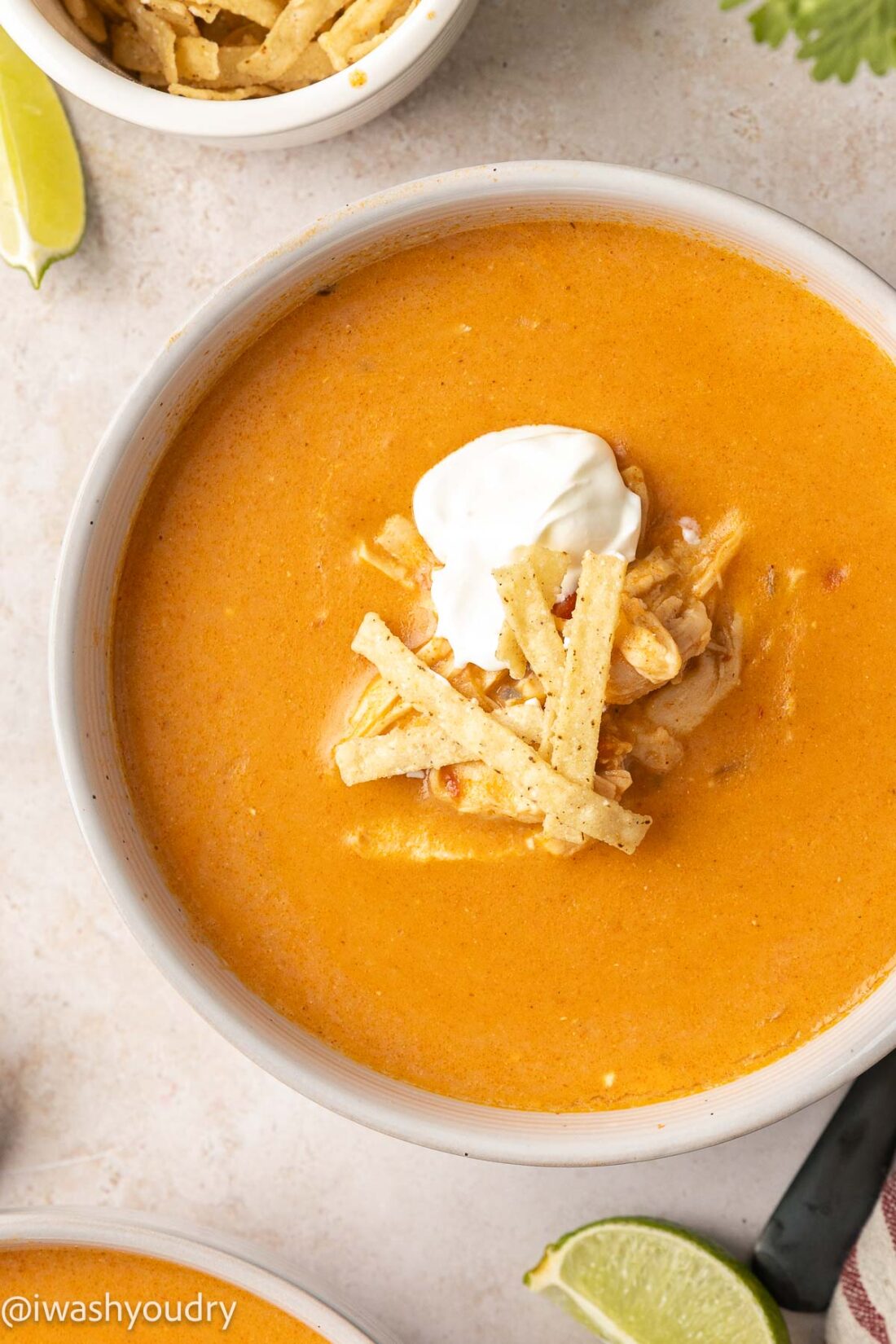 bowl of chicken enchilada soup with tortilla strips on top and a dollop of sour cream.