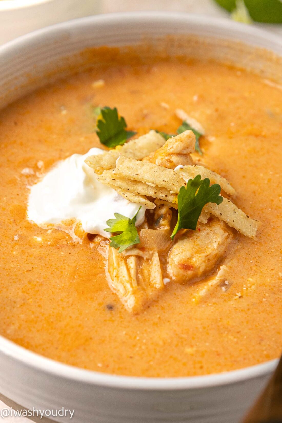 creamy chicken enchilada soup in white bowl with sour cream and tortilla strips on top.