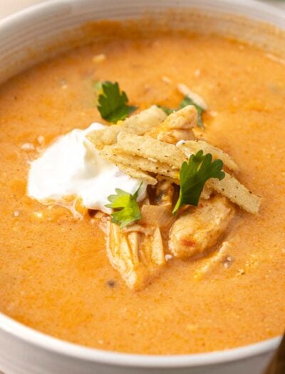 creamy chicken enchilada soup in white bowl with sour cream and tortilla strips on top.