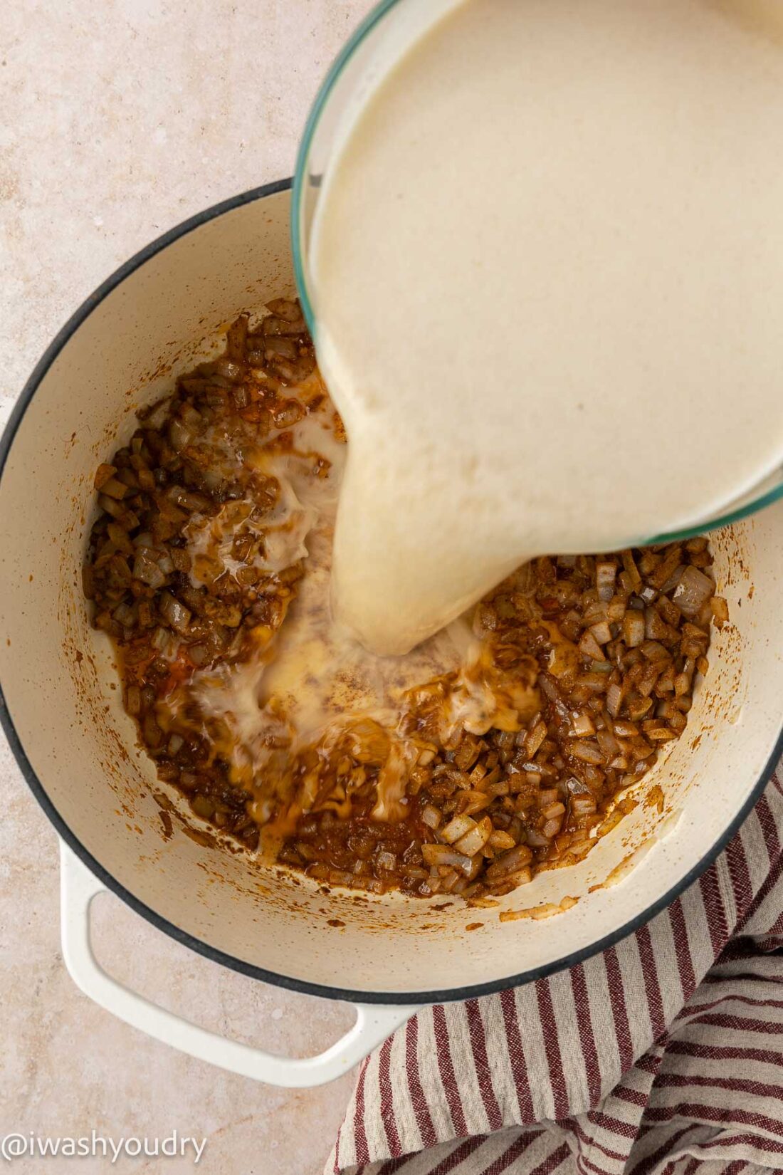 pouring creamy corn flour mixture into sauteed onions for enchilada soup base.