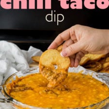 A glass bowl of dip with a hand dipping a bagel shaped chip in it